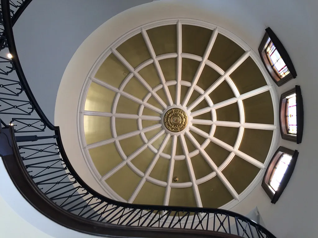 Winding staircase with gold arched ceiling and three windows